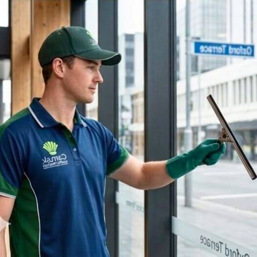 Professional cleaner from CAMAK Services Limited cleaning glass windows in a modern commercial building.